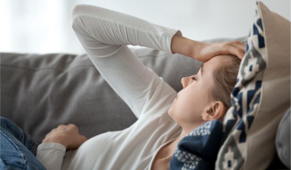 Erschöpfte Frau liegt auf der Couch und hält eine Hand an den Kopf