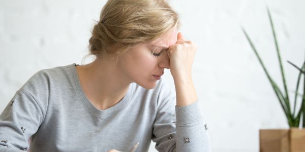 Erschöpfte Frau sitz am Tisch über einem Buch und stützt den Kopf auf die Hand