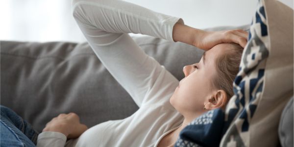 Erschöpfte Frau liegt auf der Couch und hält eine Hand an den Kopf