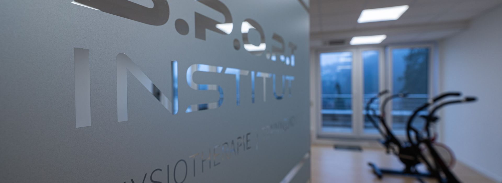 Nahaufnahme einer Glastür zum Trainingsraum mit Geräten im Hintergrund