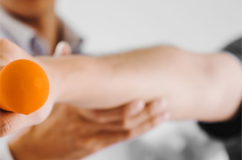 Mann hält am ausgestreckten Arm ein Gewicht und wird von Physiotherapeuten angeleitet