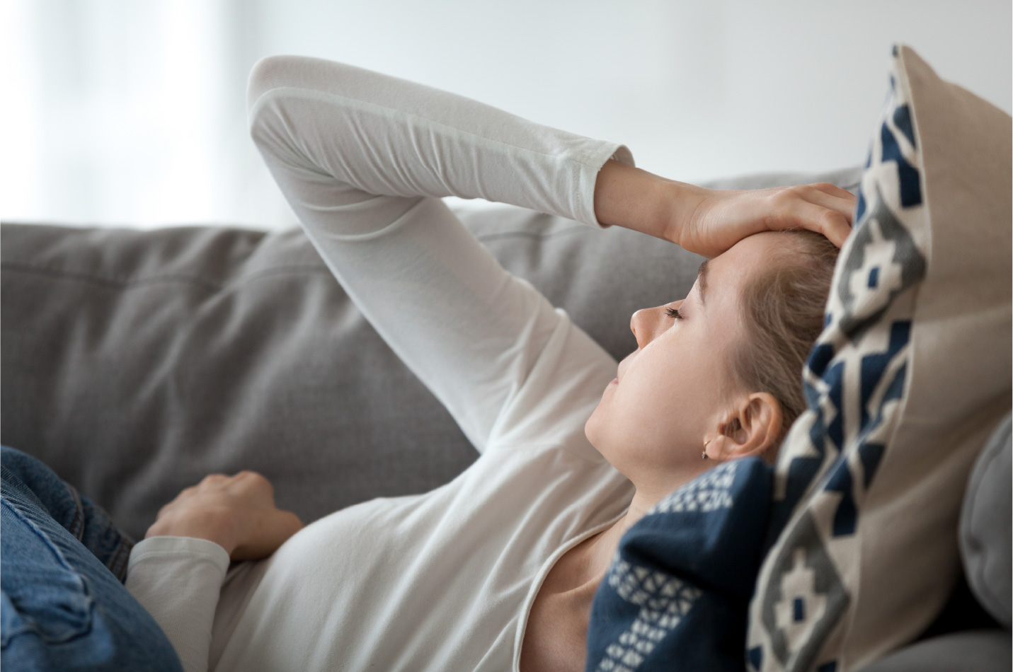 Erschöpfte Frau liegt auf der Couch und hält eine Hand an den Kopf